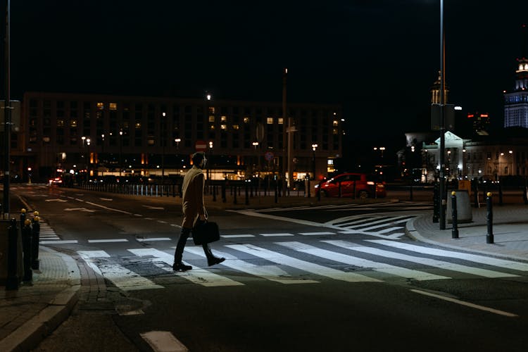 A Person Carrying Briefcase Crossing A Pedestrian Lane At Night