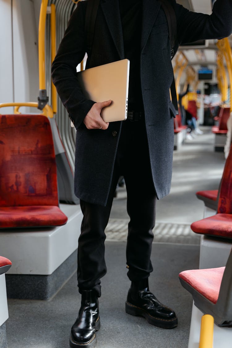 A Person In Black Coat Holding A Laptop Standing On A Train's Aisle