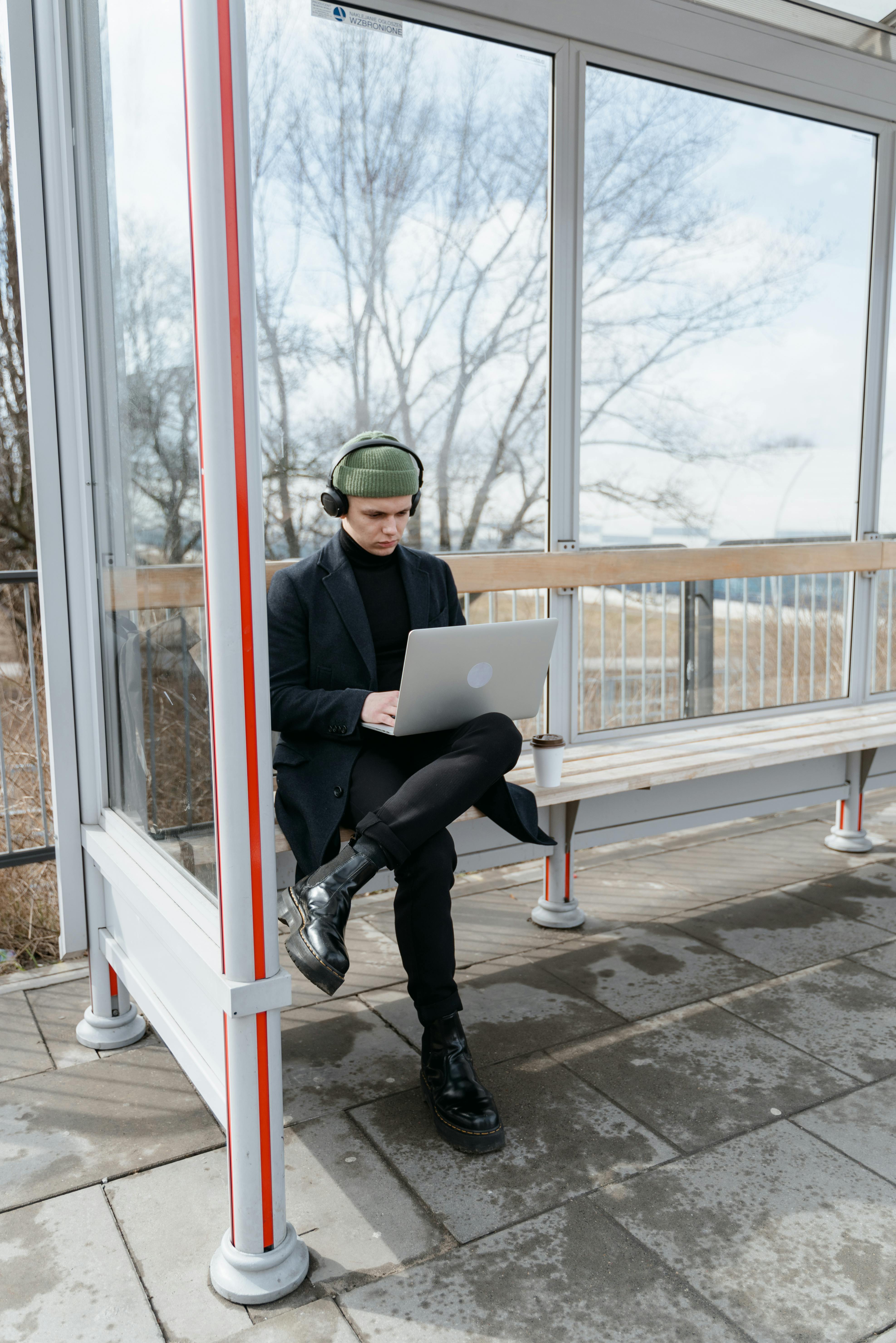 a man using a laptop while waiting on a bus stop