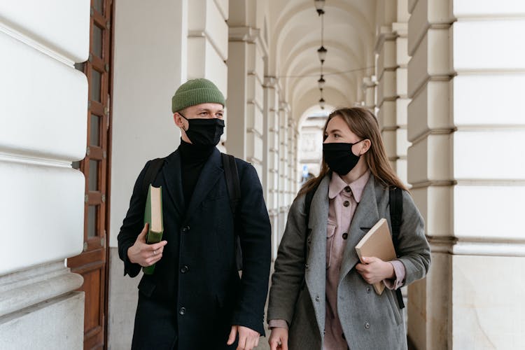 

A Man And A Woman In Face Masks Walking On A Hallway