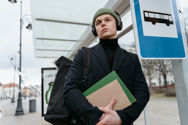 A Man With Headphones Over A Knit Cap Beside A Bus Signage