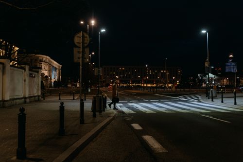 Free A person crossing a city street at night, illuminated by street lights in an urban setting. Stock Photo