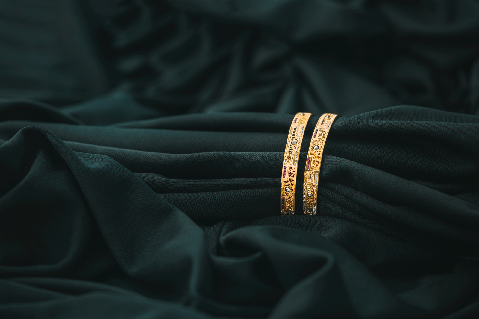 Stacked gold bangles on dark fabric