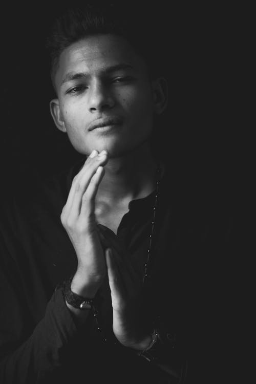 Black and white of young ethnic male looking at camera on black background of studio
