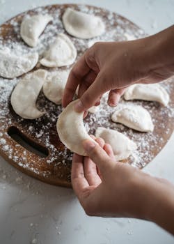 Close-up of hands making dumplings with flour on a wooden board.