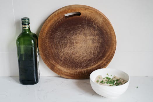 A rustic kitchen setup featuring dumplings in a bowl and an oil bottle next to a wooden cutting board.