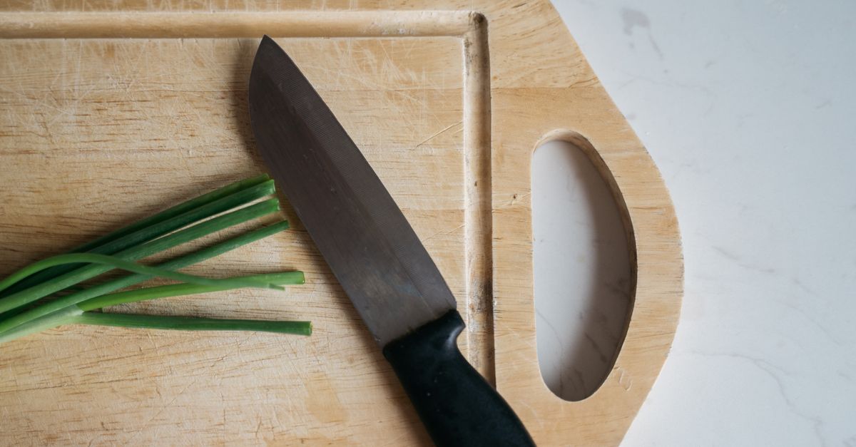 Couteau de chef posé sur une planche à découper en bois avec des oignons verts