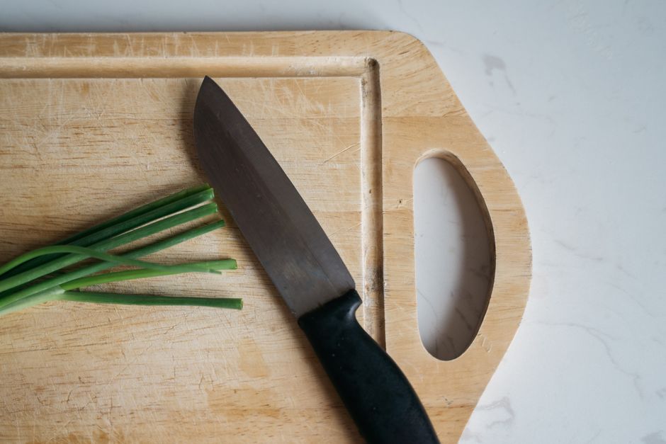 Close-up of a knife on a wooden cutting board with green onions. Ideal for kitchen and cooking themes.
