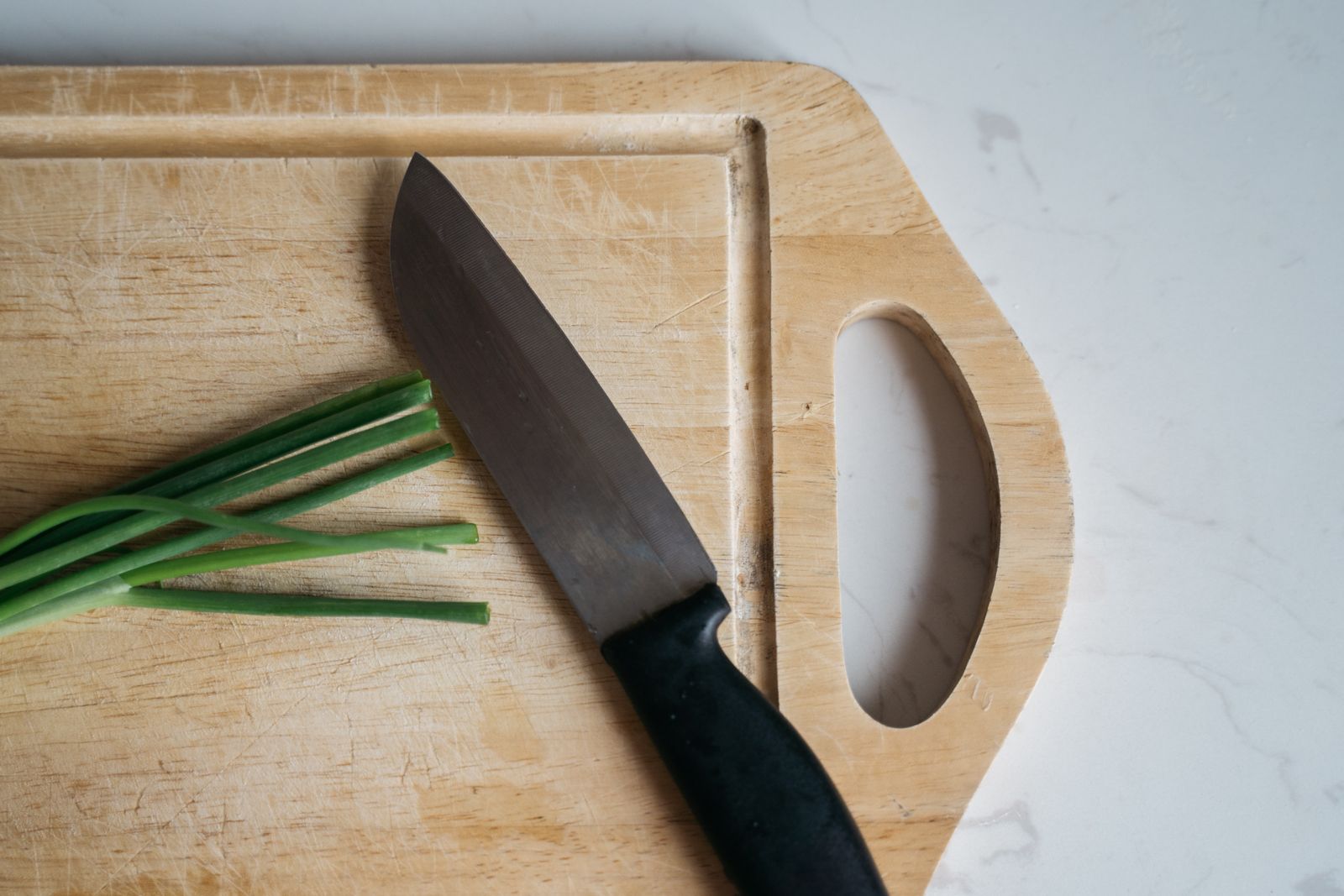 Close-up of a knife on a wooden chopping board with green onions