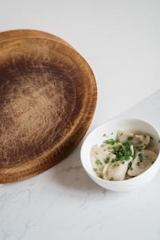 A bowl of dumplings garnished with fresh chives on a rustic wooden table.