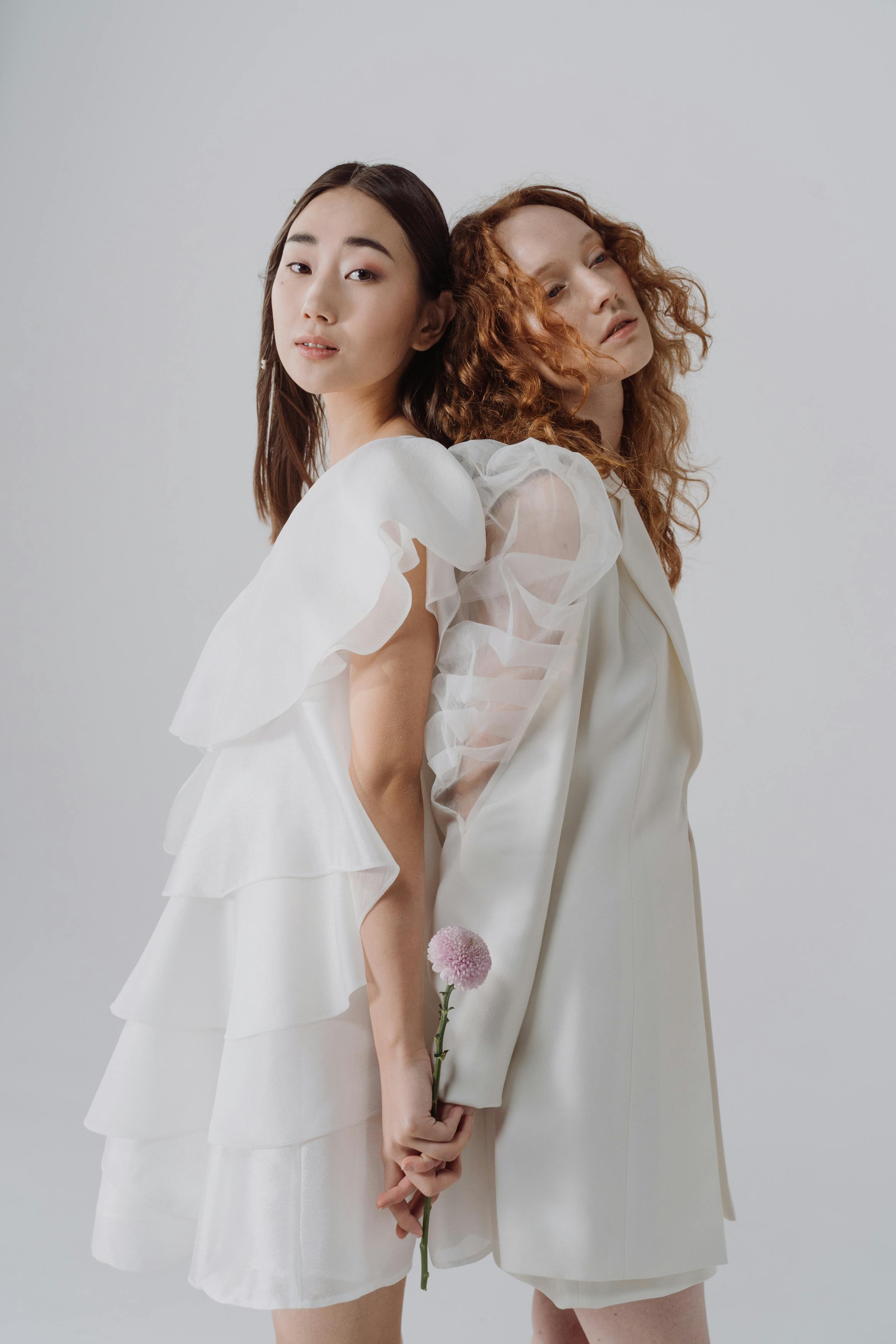 women in white dress standing back to back while holding hands