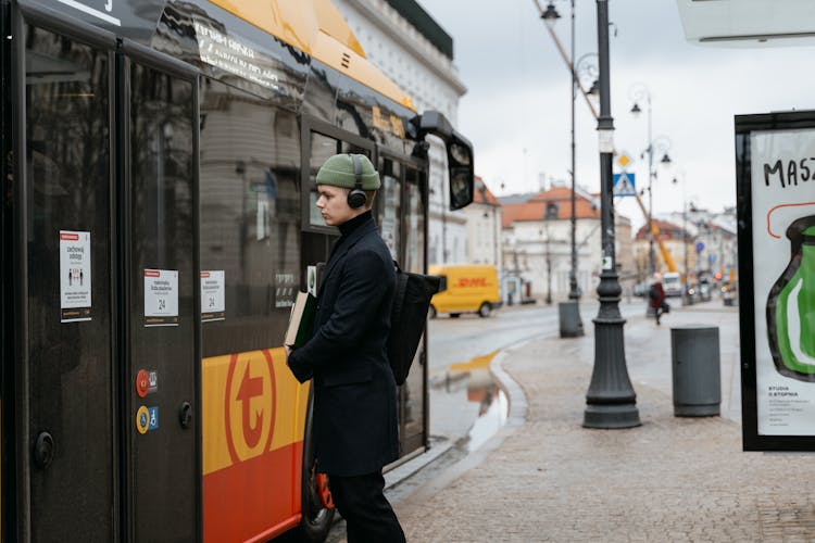 A Man In Black Coat Standing Near The Bus While Wearing Headphones