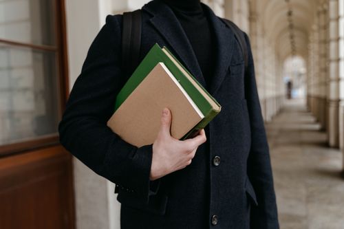 Free An individual in a coat holds books in an elegant indoor setting with arched architecture. Stock Photo
