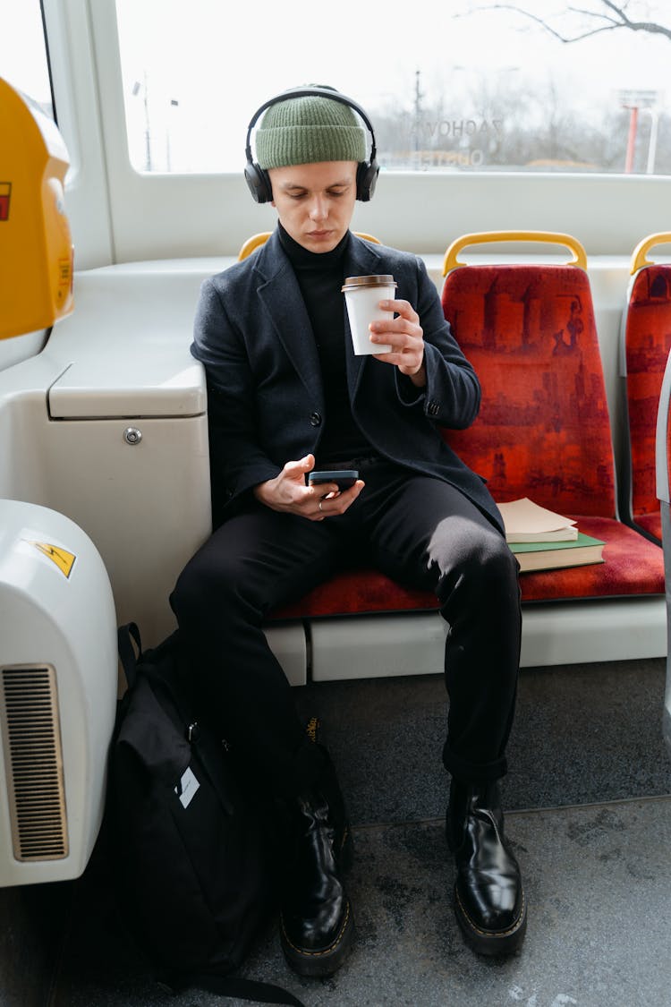 A Man In Gray Coat Sitting On The Bus While Using His Phone