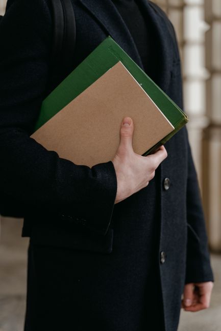 Close-up of an adult holding folders in a suit jacket, indoors, academic setting. Close-up of an adult holding folders in a suit jacket, indoors, academic setting.