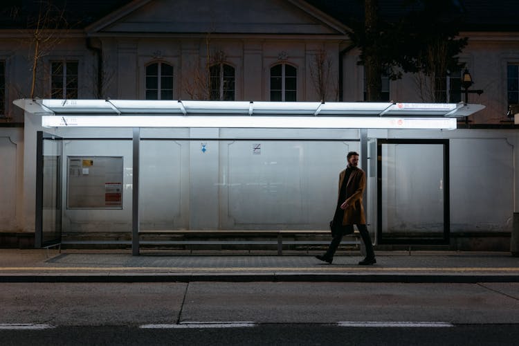 A Man Walking On The Sidewalk At Night