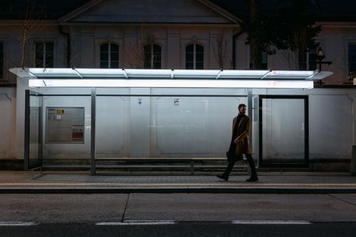 Free A man walks past a lit bus stop at night, creating a moody urban scene. Stock Photo