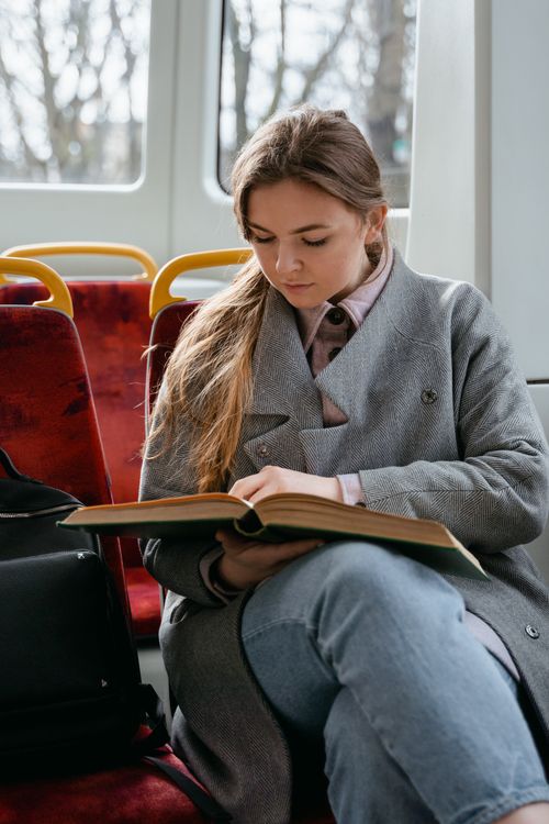 Free Caucasian woman in a gray coat reading a book on a tram. Urban commuting scene. Stock Photo
