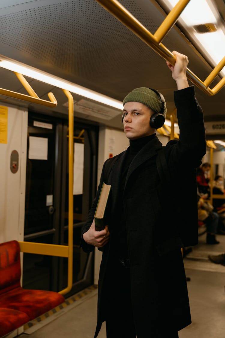 A Man In Black Coat Standing Inside The Train While Holding On Handrail