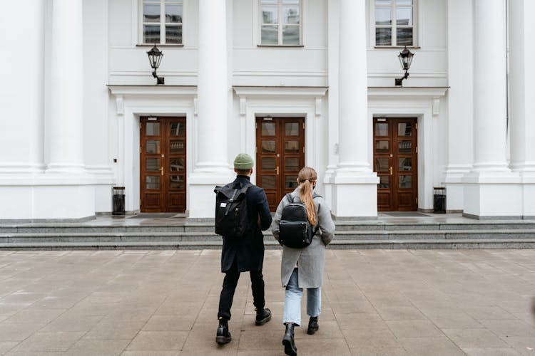 A Man And Woman Walking In Front Of A Concrete Building