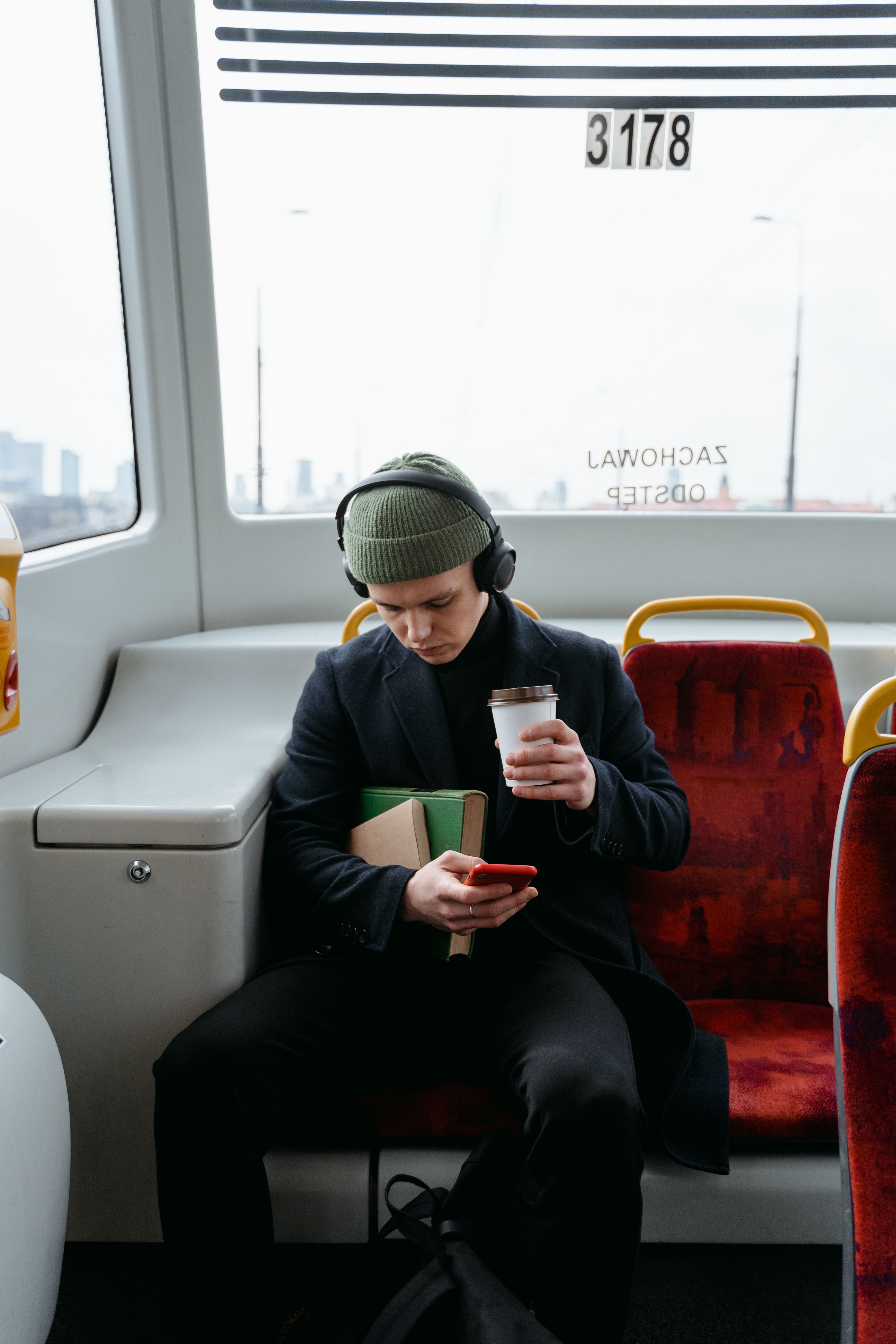Man in black coat with coffee and book enjoying a quiet tram ride.