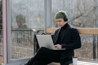 A Man in Black Coat Using a Laptop while Using a Wooden Bench