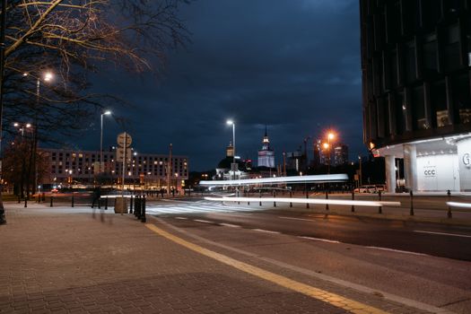 City street at night with light trails and buildings under a dark sky.