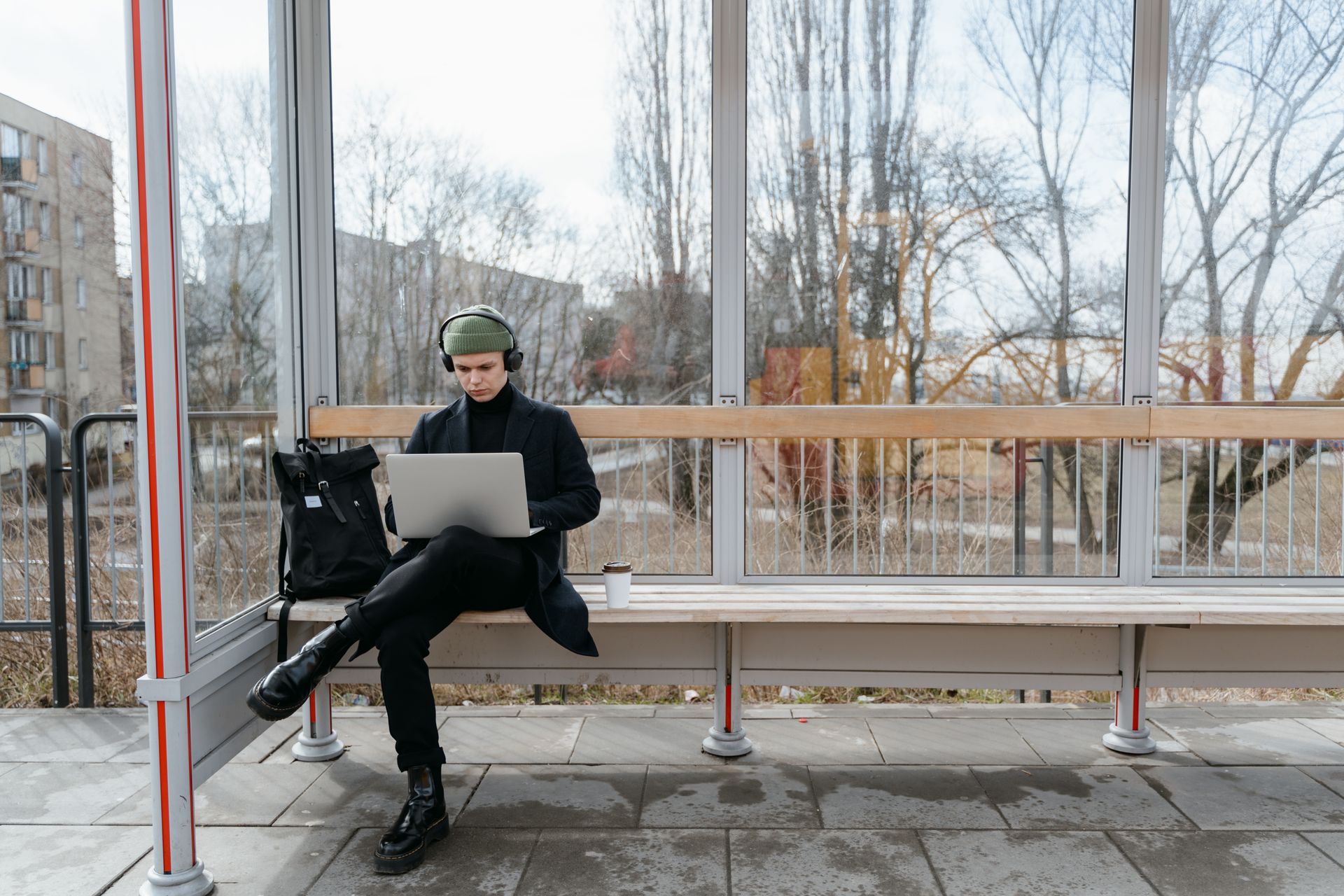 A Man Waiting at a Bus Stop while Using His Laptop