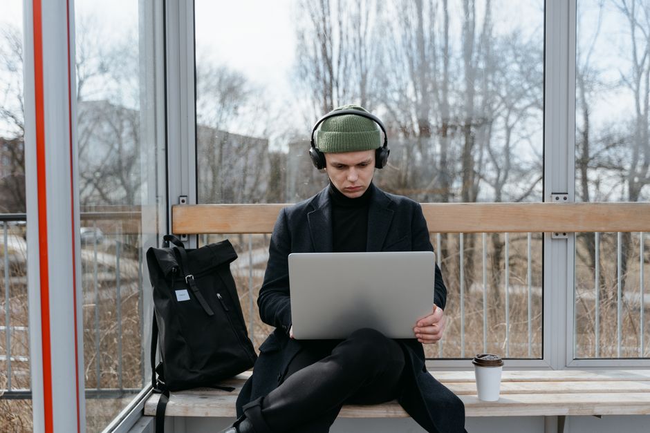 Man sitting at a bus stop working on a laptop, embracing remote work lifestyle. Man sitting at a bus stop working on a laptop, embracing remote work lifestyle.