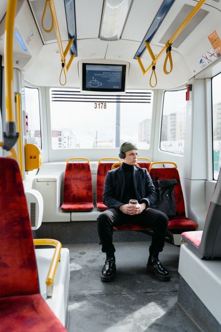 Man with headphones and beanie holding a cup, sitting in a modern train interior, commuting.