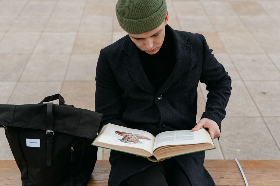 Young man in a green beanie reading a book outdoors, enjoying leisure time on a bench. Young man in a green beanie reading a book outdoors, enjoying leisure time on a bench.