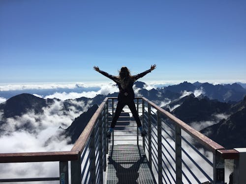 Free Person Standing on Hand Rails With Arms Wide Open Facing the Mountains and Clouds Stock Photo