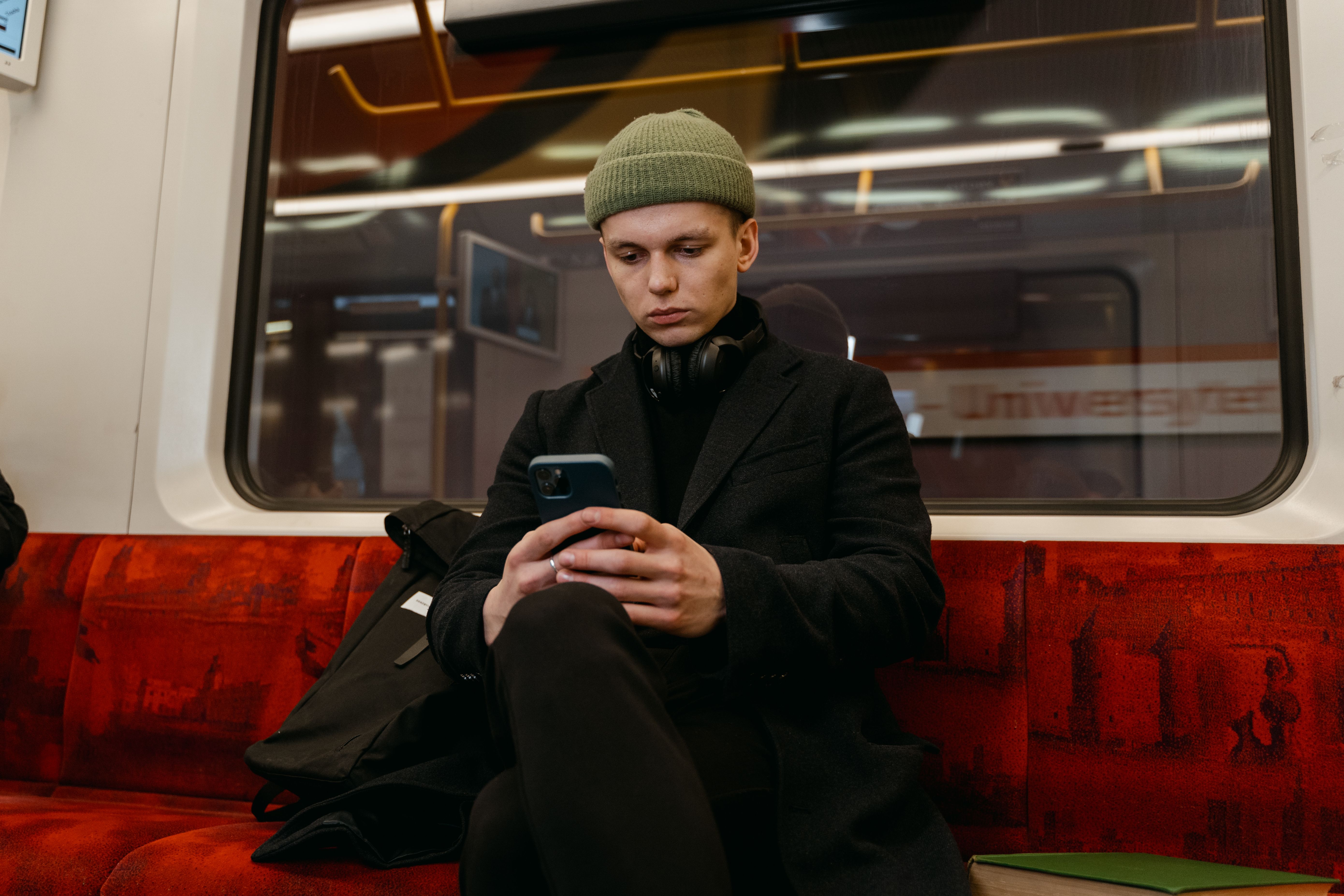 Man in beanie and black coat using smartphone while commuting on subway.