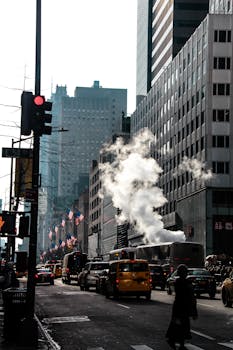 A bustling New York City street with steam, traffic, and iconic skyscrapers at daytime.
