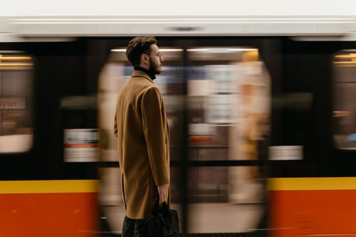 Free A man with a beard stands in focus against a moving train background at a station. Stock Photo