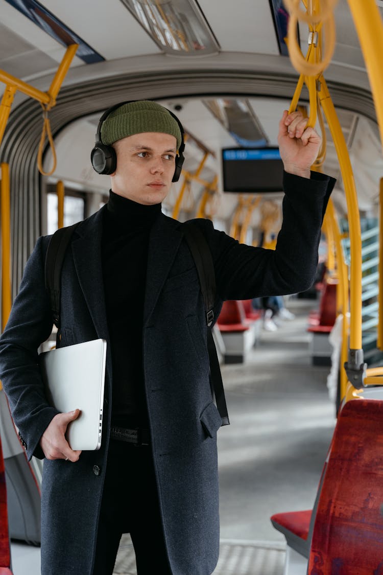 A Man With Headphones Holding Onto A Train Handle