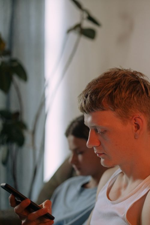 Free Two young adults focused on their phones indoors, casual and relaxed atmosphere. Stock Photo