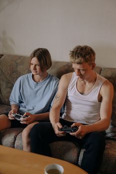 Two young adults playing video games together indoors on a cozy couch.