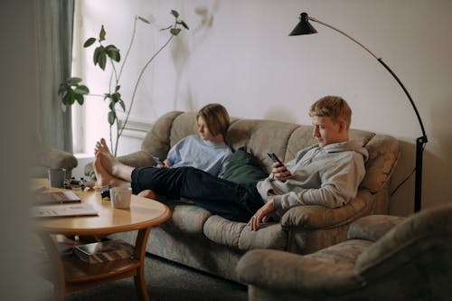 Man and Woman Sitting on Brown Couch Using Cellphone