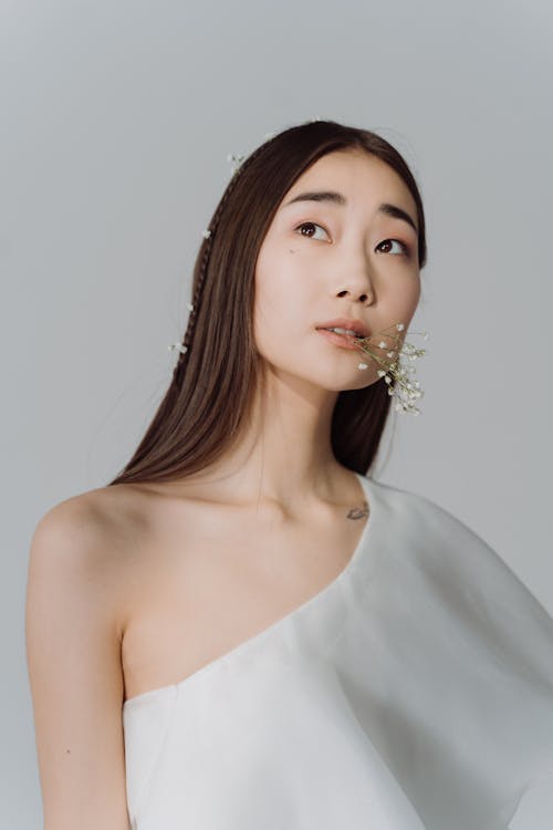 A Woman in White Top Biting on a Stem of Baby's Breath