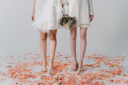 Elegant couple in white wedding attire holding a bouquet, standing on a petal-covered floor.