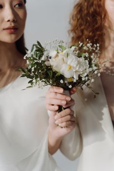 Close-up of women in white attire holding a delicate bouquet with white flowers and greenery.