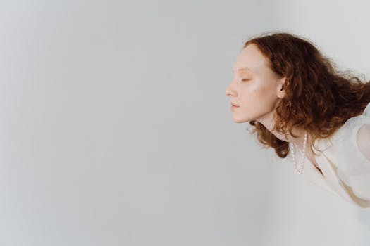 Minimalistic side portrait of a woman with red hair, eyes closed, and wearing a pearl necklace, against a white background.