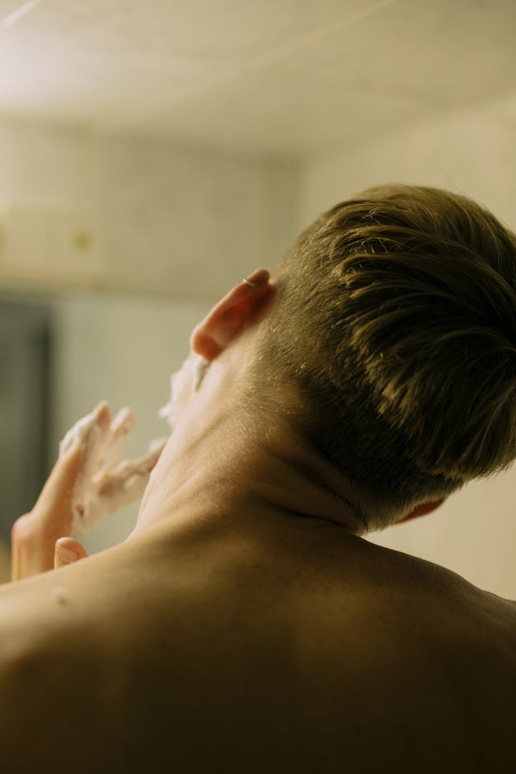 A Shirtless Person With Cream On Fingers Tilting His Head Sideways