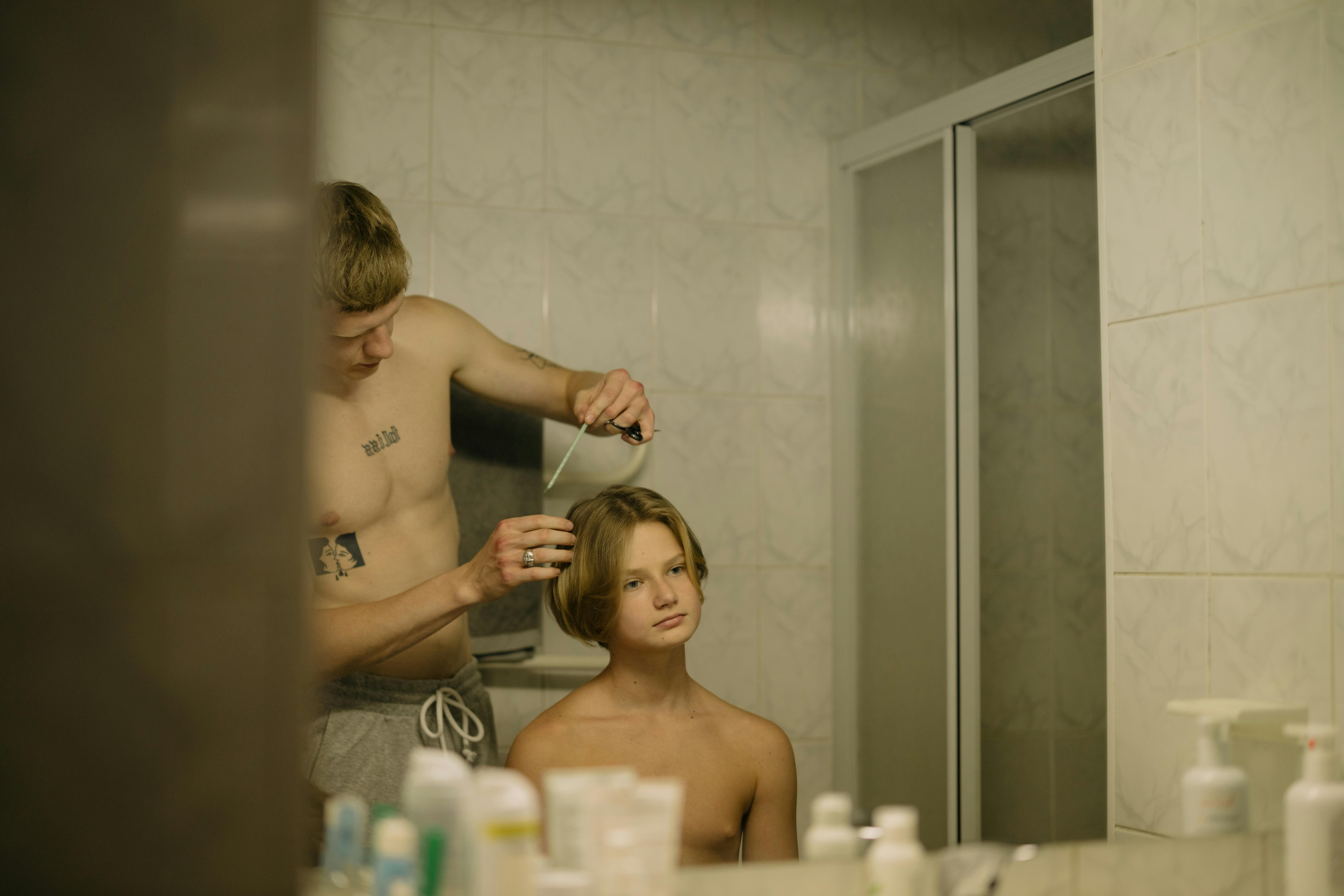 A Shirtless Young Man Having a Haircut in the Bathroom · Free Stock Photo