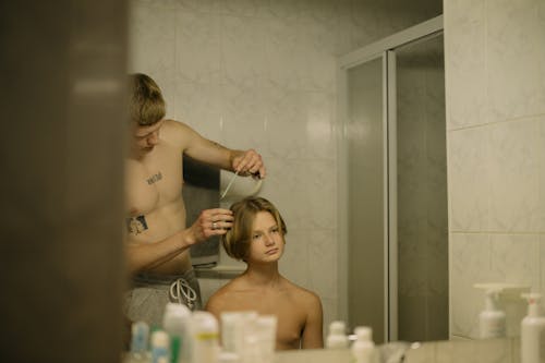 A Shirtless Young  Man Having a Haircut in the Bathroom