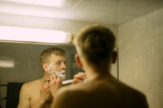 Adult man shaving in a bathroom mirror, highlighting daily grooming routine.