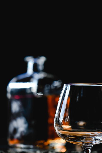 A short glass of amber apple brandy next to a wooden bowl of fresh apples and a cinnamon stick