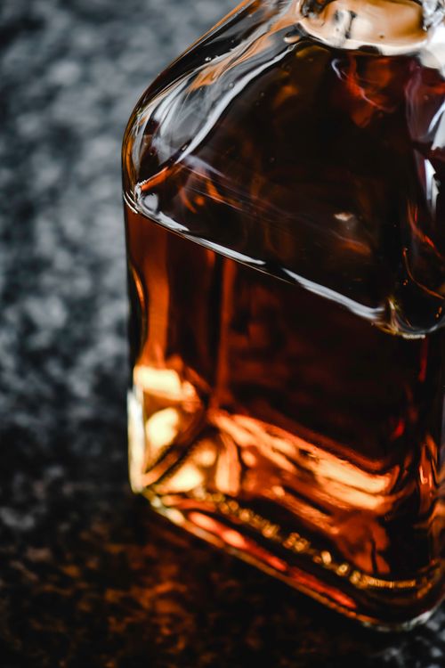 Free Close-up of a whiskey bottle on a dark background, showcasing elegant glass and amber tones. Stock Photo