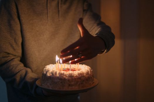 Person holding a birthday cake with lit candles in dim lighting, creating a warm celebratory atmosphere.